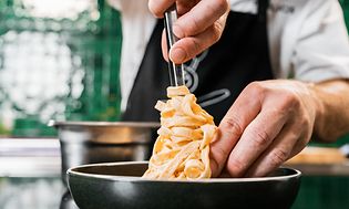 kok i færd med at arrangere pasta i en dyb tallerken