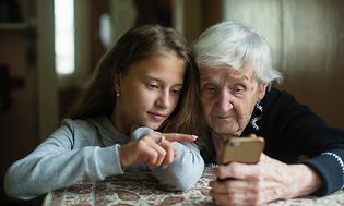 Billede af en gammel kvinde og en pige der bruger en telefon
