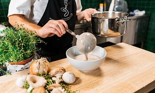 Kok hælder grøntsagssuppe op i en skål fra en gryde