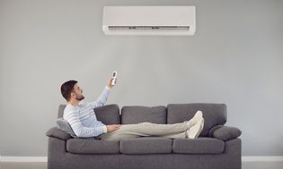 Mand på en sofa med en fjernbetjening i hånden under en varmepumpe