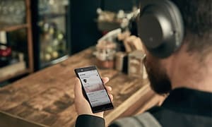 Mand i en cafe iført hovedtelefoner, holder en smartphone 