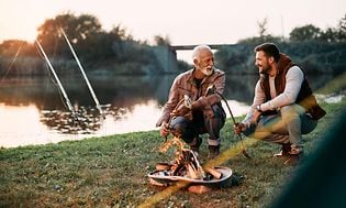 To mænd der griller over et bål ved en flod