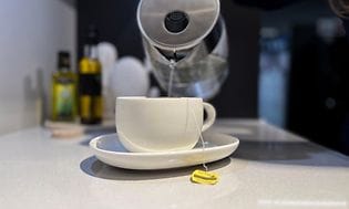 Elkeddel der hælder varmt vand op i en kop på et køkkenbord