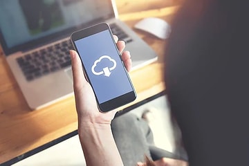 Telecom - skift fra iPhone til Android - Person der holder en telefon i hånden der downloader fra skyen