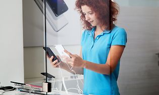 Telecom - Skift telefoner - En kvinde der sammenligner telefoner i en butik