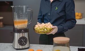 SDA - Blender - En kvinde der holder et fad med frugt ved siden af en blender