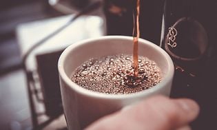 En kop kaffe bliver skænket fra en kaffemaskine