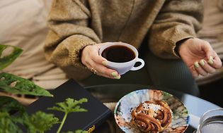 En kvinde nyder en kop kaffe og en kanelbolle