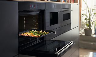 Bosch Accent line oven with the door open and a baking tray with vegetables