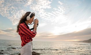Ung kvinde på stranden iført hvide Bose høretelefoner