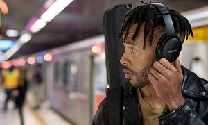 Ung mand på en togstation iført sorte Bose høretelefoner