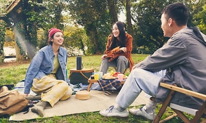 En gruppe mennesker på en picnic i parken med en bærbar højttaler i mellem dem