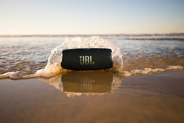 JBL Charge 5 på strandkanten med en bølge over sig