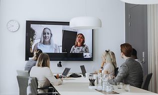 Mennesker der sidder til et møde foran en storskærm og laptops