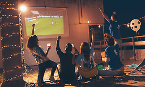 Hjemmebiograf: En gruppe venner, der ser sport på en projektor udendørs.