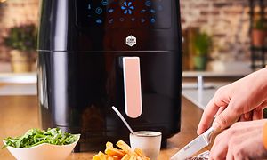 SDA - Household - OBH Nordica EasyFry bag ved person der skærer i en steak ved siden af pommes og grøntsager