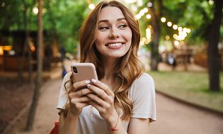 Smilende kvinde med smartphone i hænderne