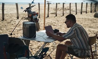 Mand der arbejder på en strand med sine enheder koblet op til en powerstation