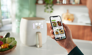 Hvid Philips Airfryer XXL på et bord og en person, der gennemser nutriU-appen