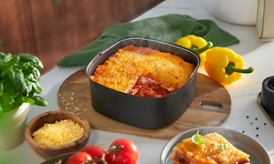 Philips Airfryers separate bageplade på et bord ved siden af en skive lasagne, friske grøntsager og basilikum