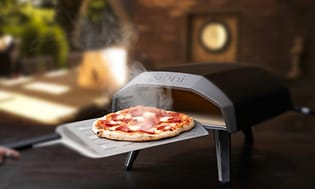 Billede af en pizza på en pizzasten foran en Ooni pizzaovn