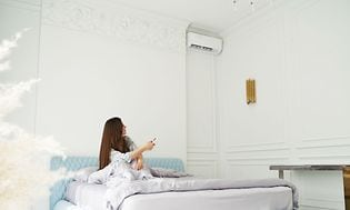 En kvinde der sidder i en seng og kontrollere en aircondition med en fjernbetjening