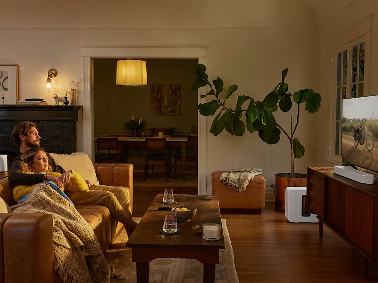 Hvid Sonos Beam 2 der står foran et tv i en stue med dæmpet belysning