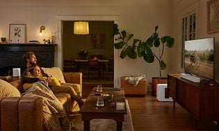 Hvid Sonos Beam 2 der står foran et tv i en stue med dæmpet belysning