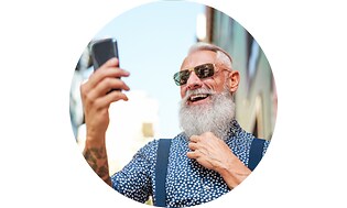 Ældre mand med skæg og solbriller der kigger på en smartphone