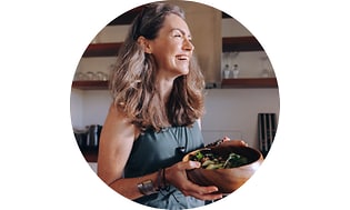 Kvinde der står og smiler med en skål salat i hænderne
