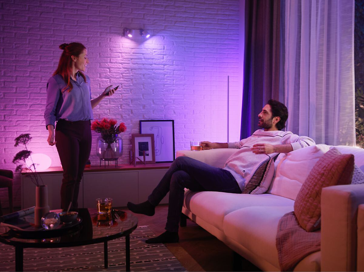 Par i en stue omgivet af lilla Philips Hue-lys og styrer det med en smartphone