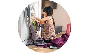 Lille pige der er ved at lægge vasketøj ind i en vaskemaskine