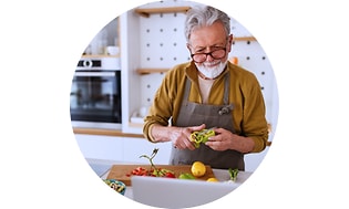 En ældre mand der står og skærer grøntsager i en køkken