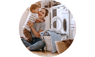 Mor der holder sit barn tæt ved en vaskemaskine og vasketøj