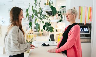 To kvinder i en butik, der står og snakker over en disk
