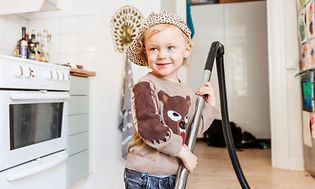 Barn der står i et køkken med en støvsuger