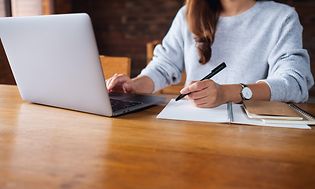 Businesskvinde arbejder på sin laptop og skriver i en notesbog