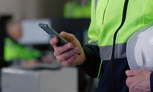Smartphone i hånden på en byggepladsarbejder