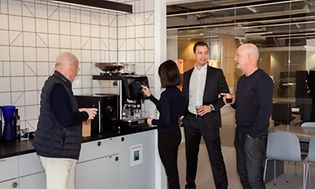 Kaffemaskine på et kontor omgivet af ansatte