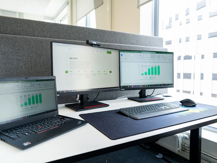 Et kontorskrivebord med laptop, skærme, mus og tastatur. 