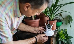 En person der sætter et overvågningskamera op på et møbel ved siden af planter