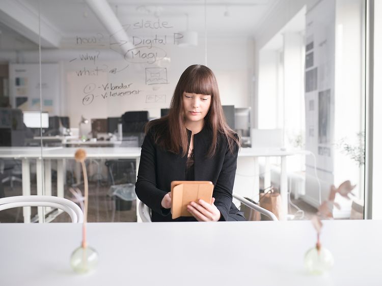 En kvinde der sidder på et kontor og bruger en tablet