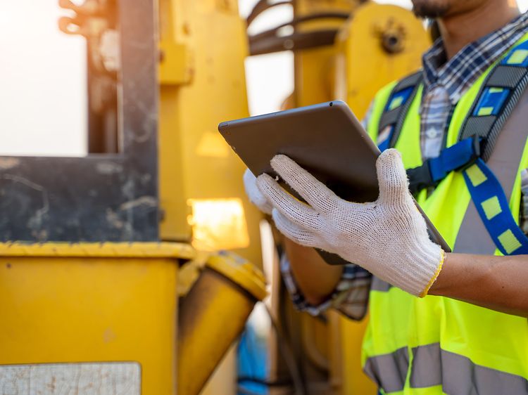 En mand der står ved en byggeplads og bruger en tablet med handsker på