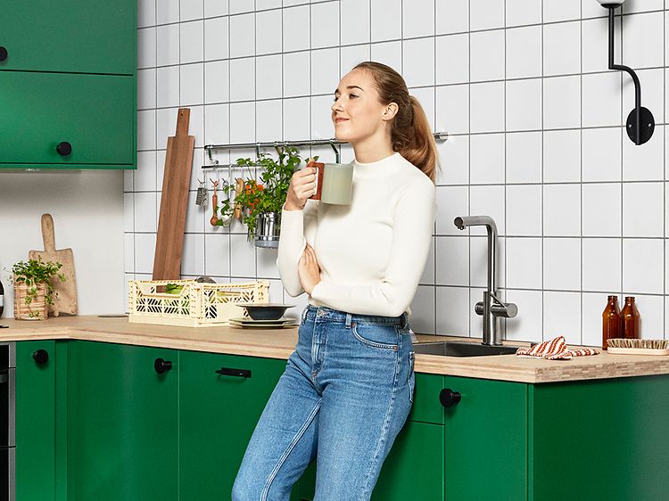 Kvinde står med et kop foran hendes grønne køkken