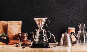 To typer kaffekander på et træbord ved siden af kaffebønner og malet kaffe