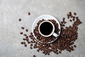 Kaffekop med bønner spredt rundt omkring på en grå bordplade