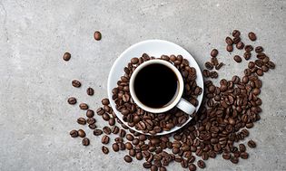 Kaffekop med bønner spredt rundt omkring på en grå bordplade