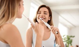Kvinde børster tænder med elektrisk tandbørste foran spejl