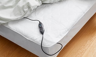 Opvarmning:  Elektrisk varmetæppe fra ReLuxury som lagen på en seng med fjernbetjening vist i hjørnet af sengen