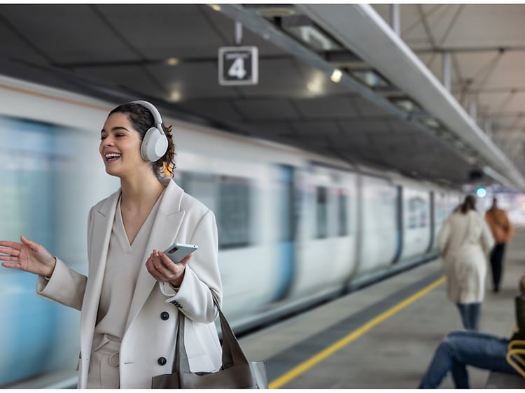 Kvinde med sony wh1000xm5 around-ear hovedtelefoner på en togstation